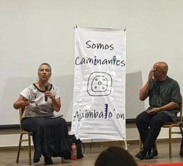 Dos personas sentadas en un evento con un cartel que dice 'Somos Caminantes'