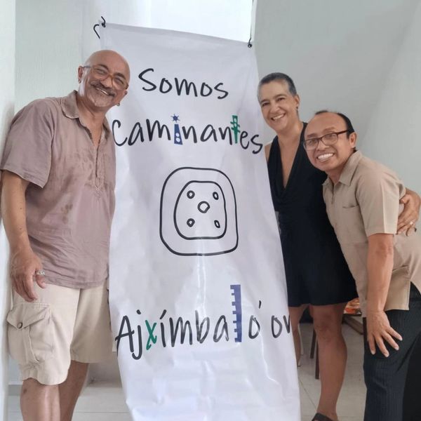 Tres personas sonrientes junto a un cartel que dice "Somos Caminantes Aximbatló'ov".