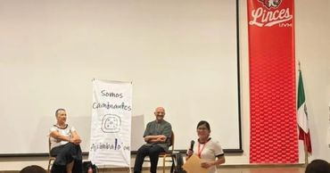 Tres personas en un auditorio frente a una pancarta que dice 'Somos Caminantes'.