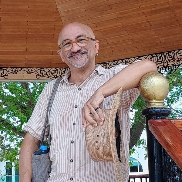 Hombre sonriente con sombrero de paja bajo un techo de madera.