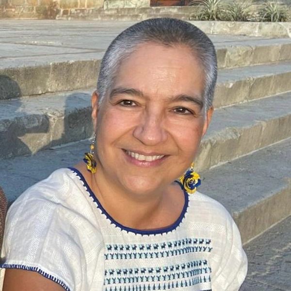 Mujer sonriente con cabello corto, usando blusa blanca bordada.