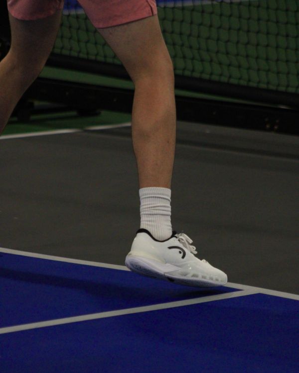 Person wearing white tennis shoes and pink shorts on court.