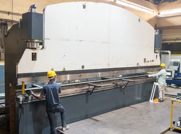 Two workers operate a large industrial metal bending machine in a factory.