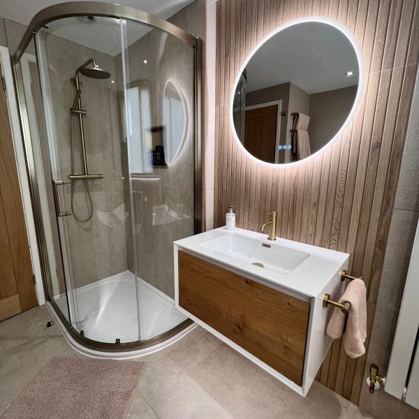Modern bathroom with glass shower and illuminated oval mirror.