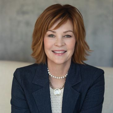 Confident woman with red hair wearing a navy blazer and pearl necklace.