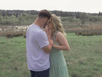 A couple sharing an intimate moment outdoors in a grassy field.