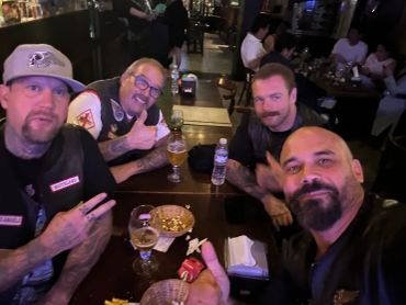 Four men at a bar table having drinks and posing for a selfie.
