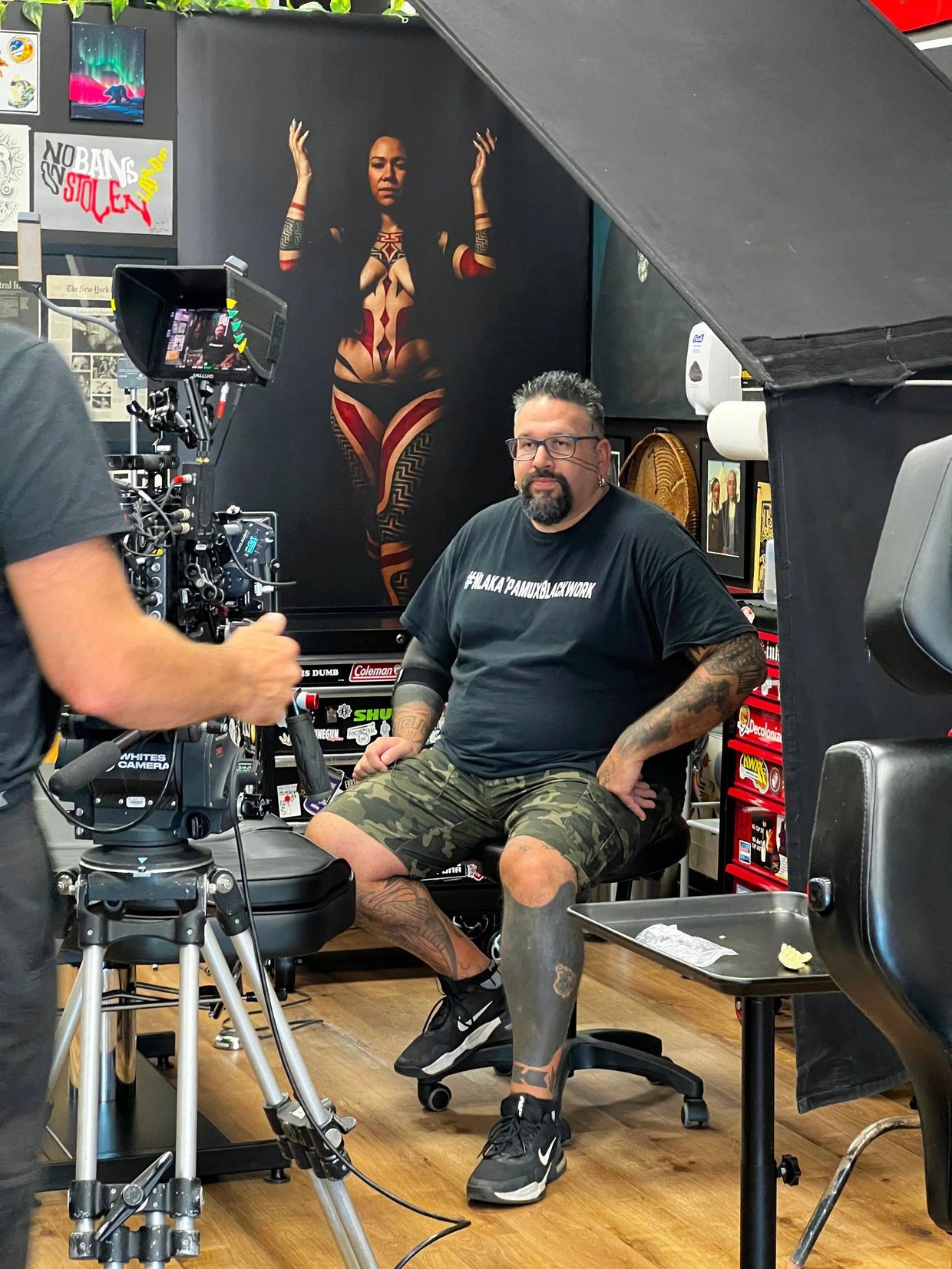 Tattoo artist sits in front of a full body portrait of beautiful woman wearing tribal bodysuit 