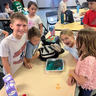 Kids excitedly gathered around a table with a colorful science project in a classroom.