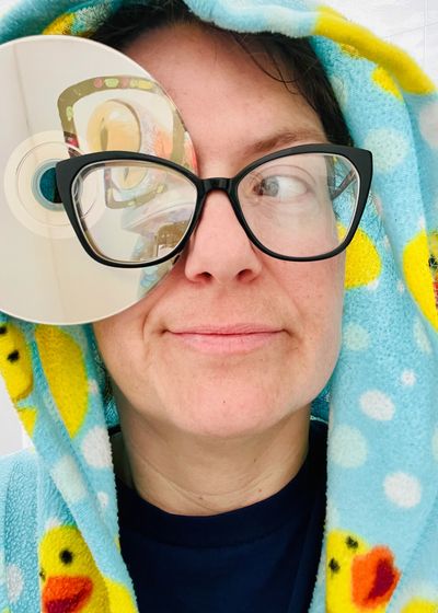 Person wearing duck-patterned robe and glasses holding a CD near their eye.