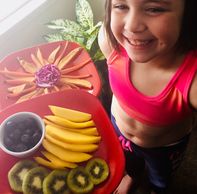 Girl smiling with a plate of sliced fruits arranged beautifully.