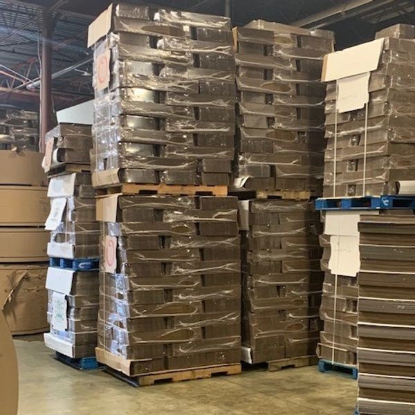Stacks of cardboard sheets wrapped on pallets in a warehouse.