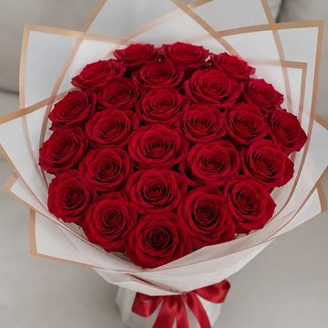 A bouquet of vibrant red roses wrapped in white and brown paper with a red ribbon.