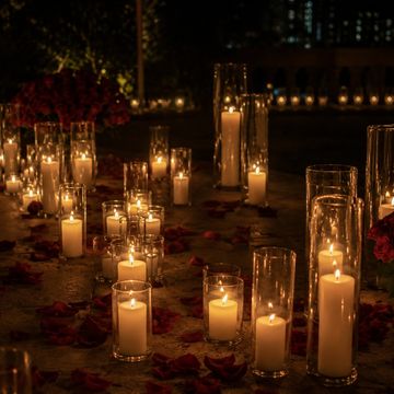 Lit candles in glass holders with rose petals scattered around in a dark setting.