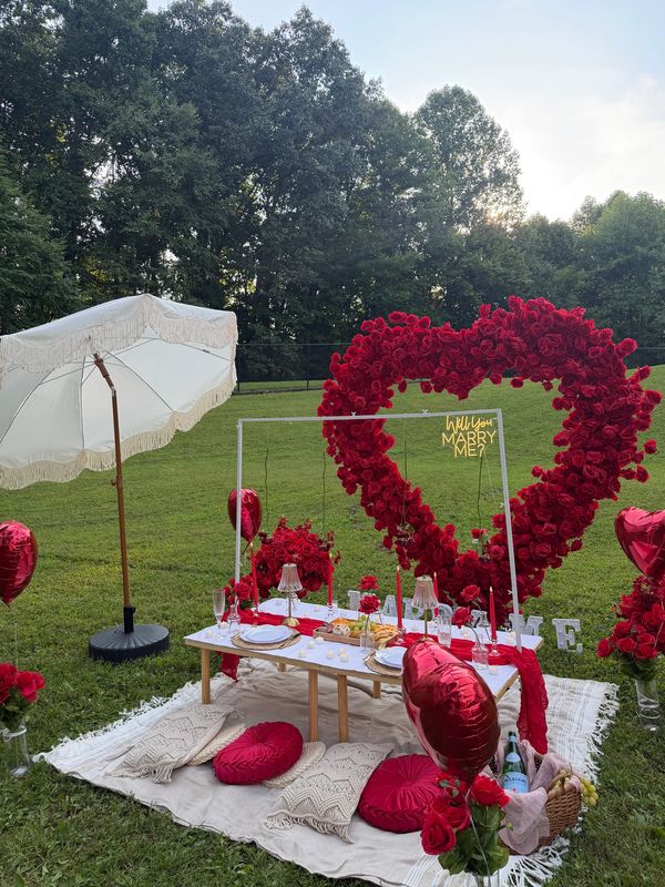 Romantic outdoor proposal setup with heart-shaped flowers and a picnic.