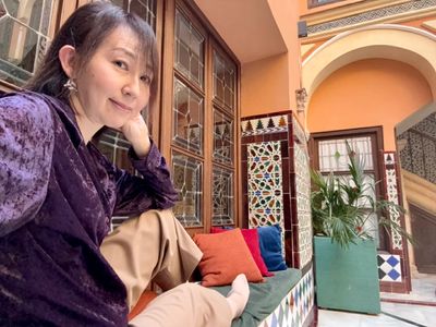 A woman in a purple top relaxing on a cushioned bench in a colorful tiled courtyard.