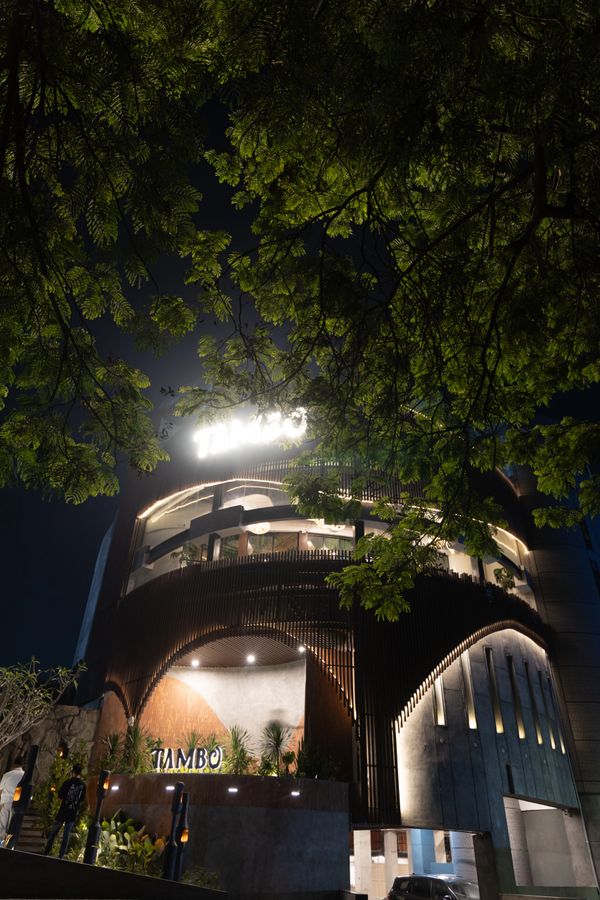 Modern building illuminated at night, framed by lush green tree branches.