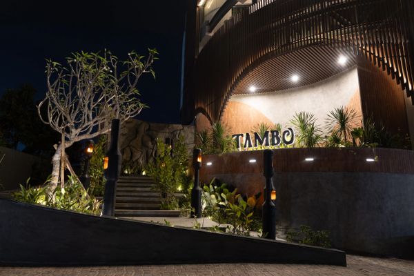 Night view of a modern building entrance with illuminated Tambo sign and lush greenery.
