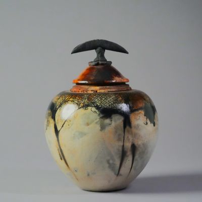 Handcrafted ceramic jar with a black and orange lid and abstract glaze.