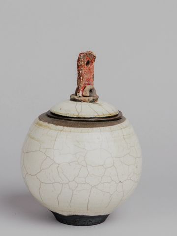 A round ceramic jar with a crackled white glaze and a lid with a red textured handle.