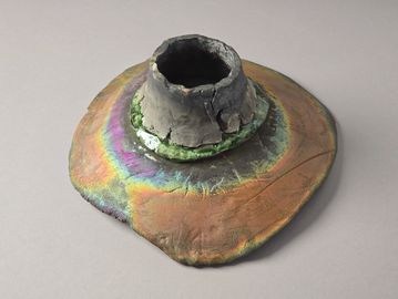 An iridescent, cracked ceramic object with a wide base and hollow center.