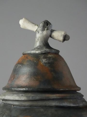 Rustic metal kettle lid with a bone-shaped handle.