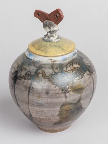 Decorative ceramic jar with abstract designs and a lid topped by a sculptural element.