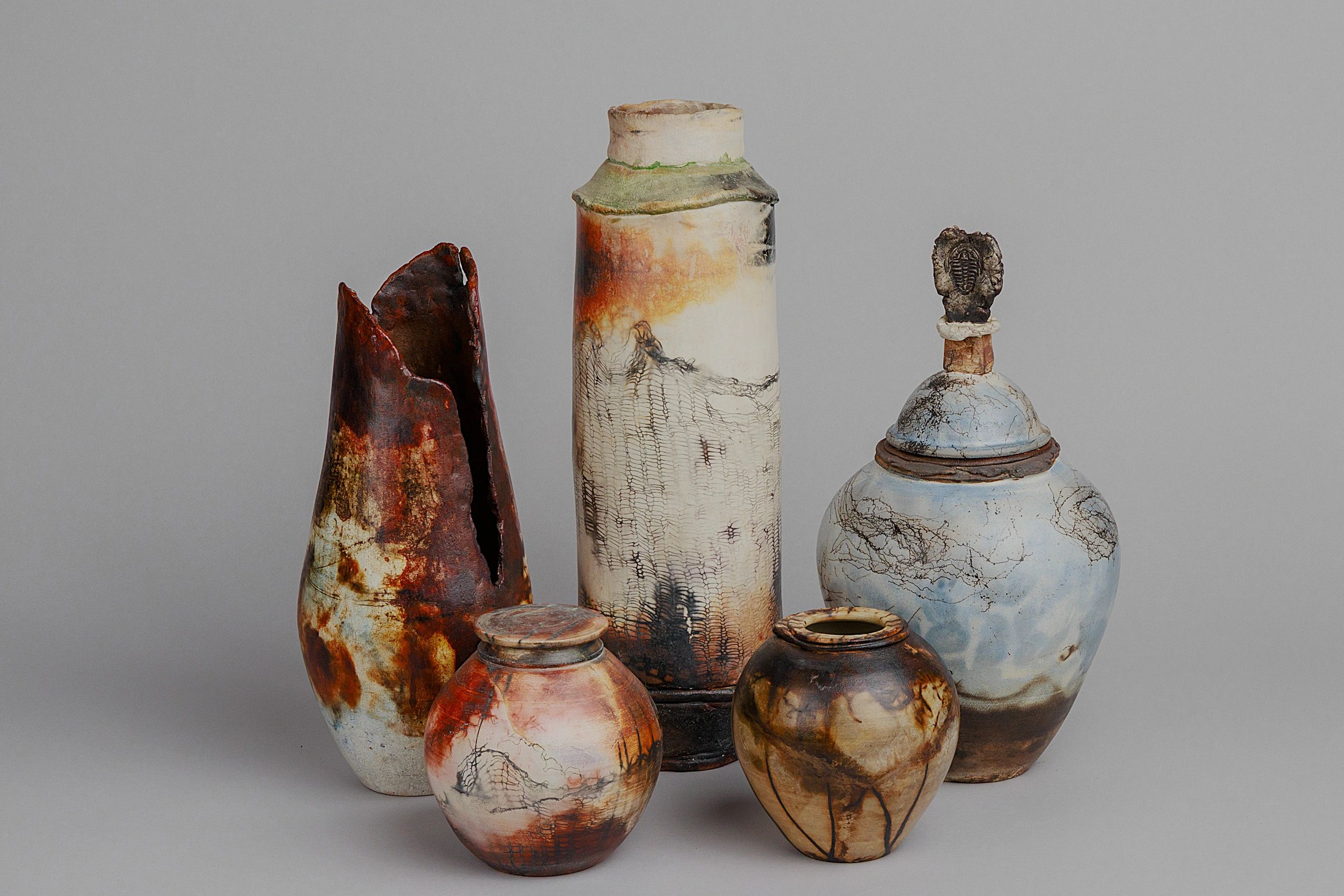 Five rustic, hand-crafted ceramic vases with earthy tones and textured designs.