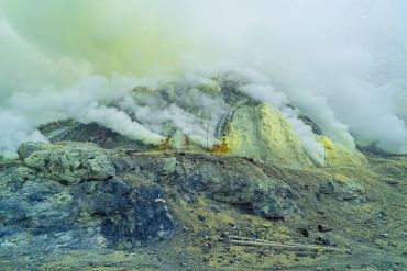 Dense smoke and sulfur fumes rise from a volcanic crater.