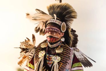 Person dressed in traditional Native American regalia with feathers and face paint.