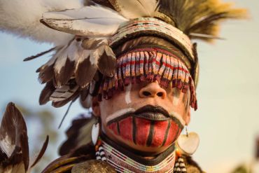 Close-up of a person in traditional tribal attire and face paint with feathers.