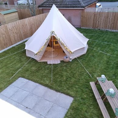 Bell tent in a garden with fairy lights on it, children's picnic benches on the grass
