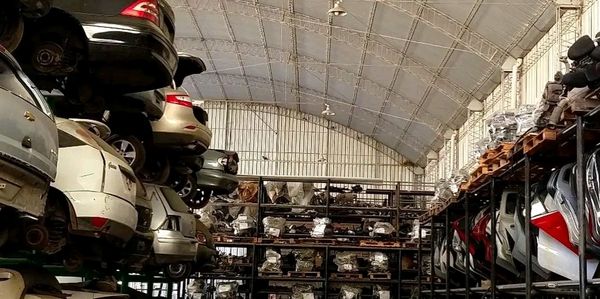 Warehouse storing stacked car parts and vehicles under a high arched roof.