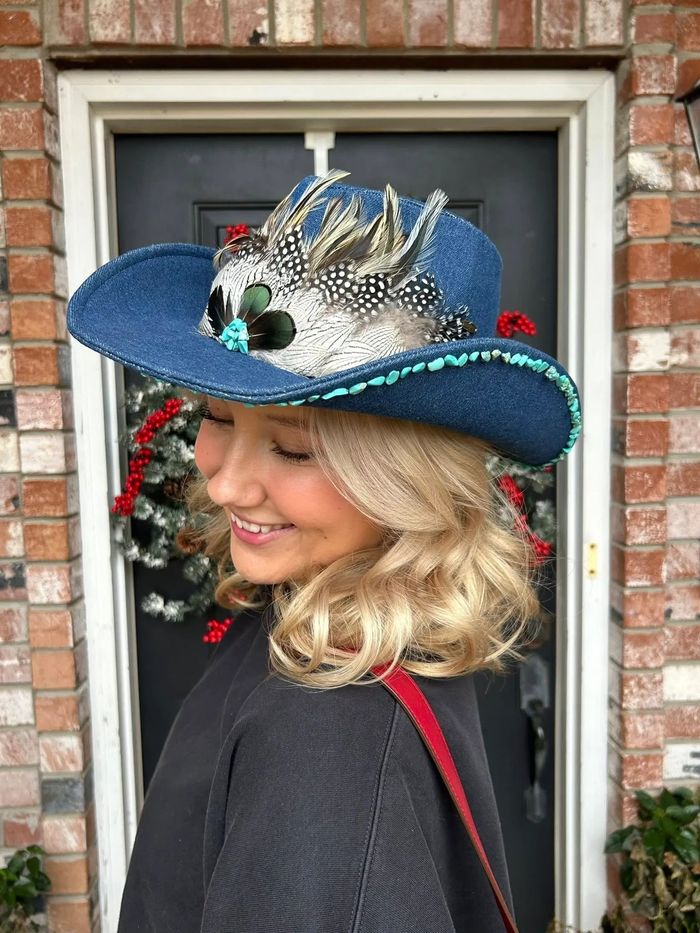 Model is wearing a denim cowboy hat with a feather pad and turquoise embellishments.