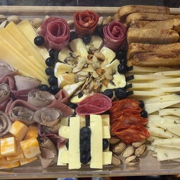A beautifully arranged charcuterie board with meats, cheeses, nuts, and breadsticks.