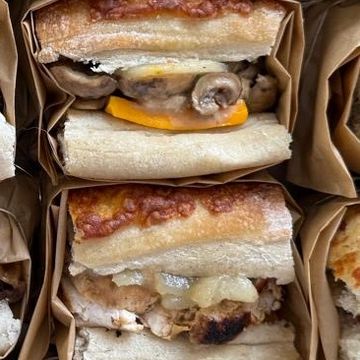 A sandwich with lettuce, tomato, and meat wrapped in brown paper.