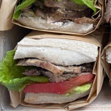 A sandwich with lettuce, tomato, and meat wrapped in brown paper.