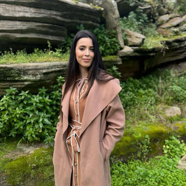 Woman in a tan coat smiling outdoors.