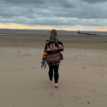 Person walking barefoot on a beach during sunset with cloudy sky.