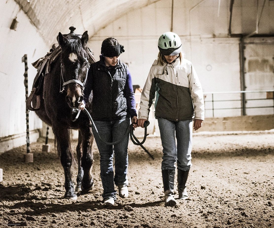 teenager and woman leading a horse in a stable