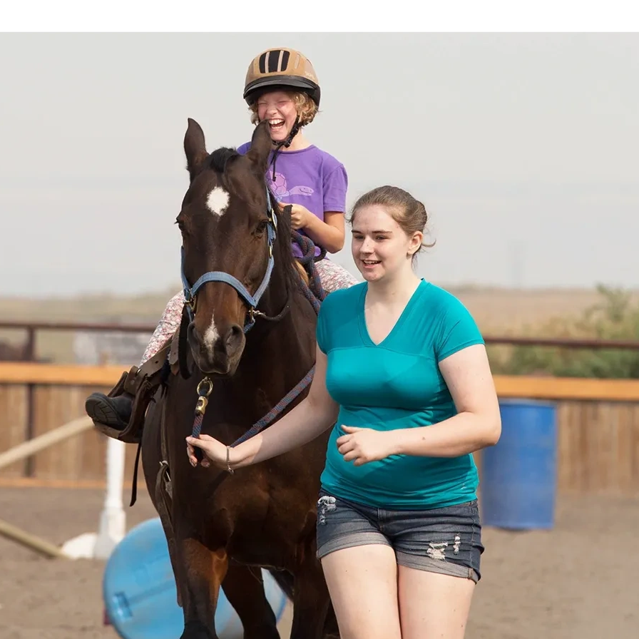 laughing child riding a horse being led by a volunteer