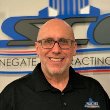 Smiling man wearing glasses and a black polo shirt with a company logo.
