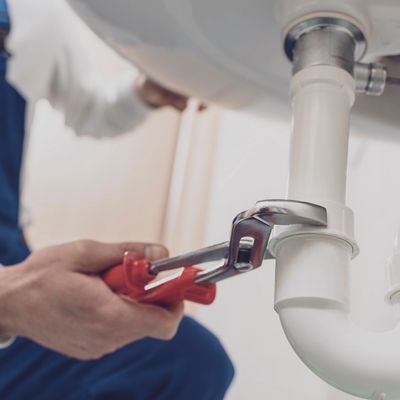Image of a plumber tightening pipe under a sink, showcasing Ellis Lake's reliable plumbing service.