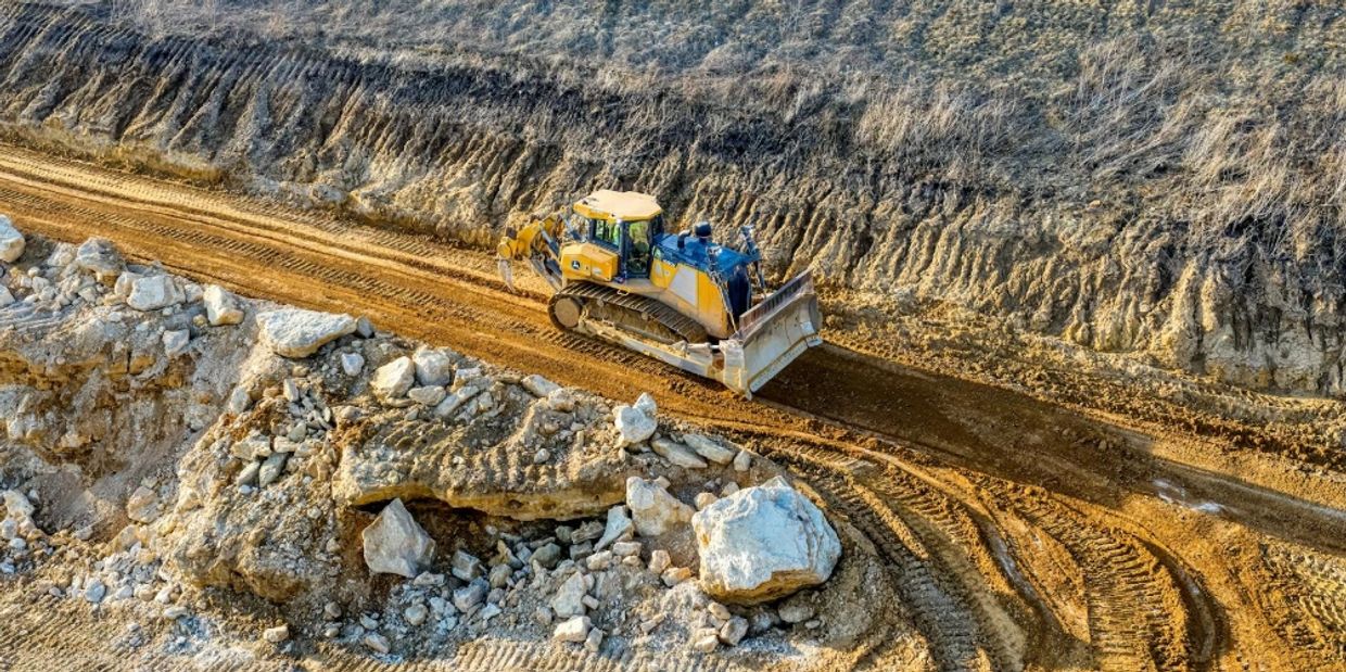 Bulldozer leveling dirt on a construction site with large rocks nearby.