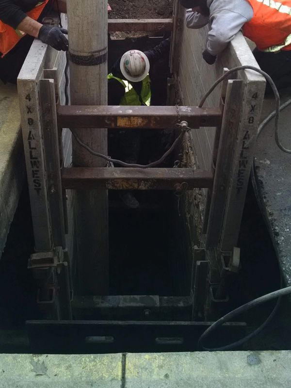 Crew repairing sewer line in deep shored trench with safety equipment and proper excavation support