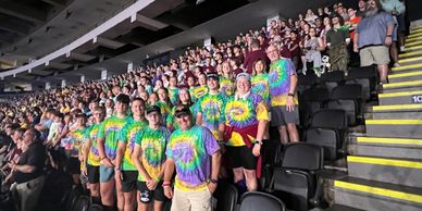 A group wearing colorful tie-dye shirts posing in a crowded stadium.