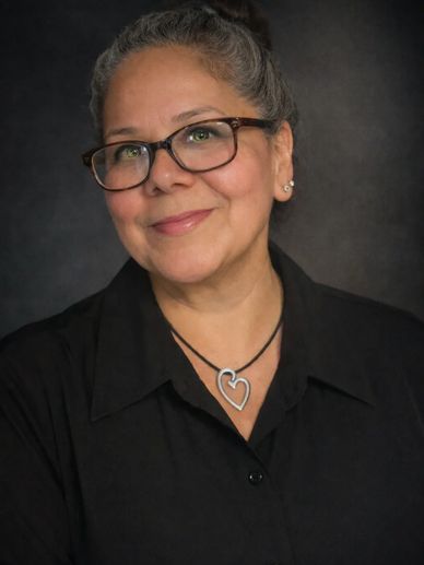 Smiling woman with glasses and heart necklace in black shirt.