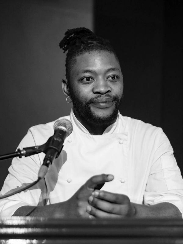 Black and white photo of a chef speaking at a microphone.
