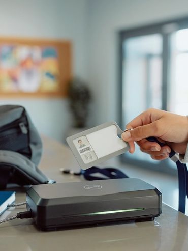 Hand holding an ID card near a scanner on a desk.