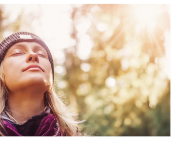 Woman enjoying the sunlight with eyes closed in a forest setting.